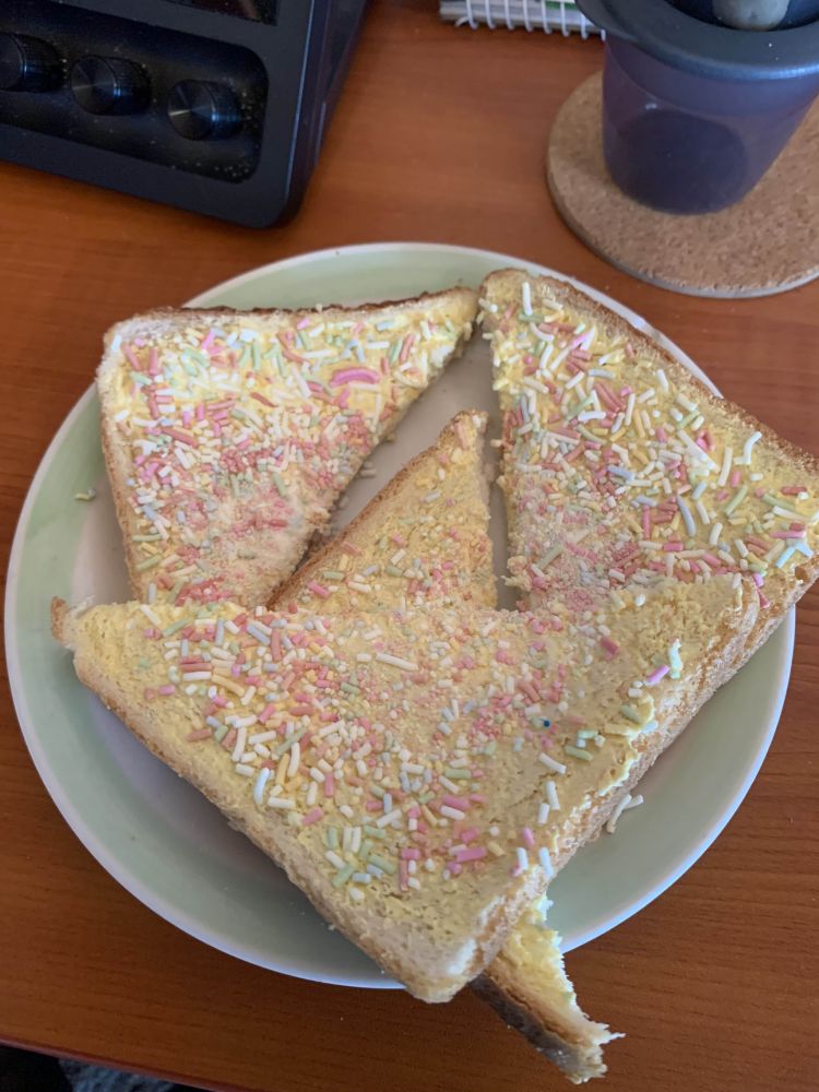 A small plate with Fairy Bread; two pieces of bread covered in butter and sprinkles, cut into triangles.