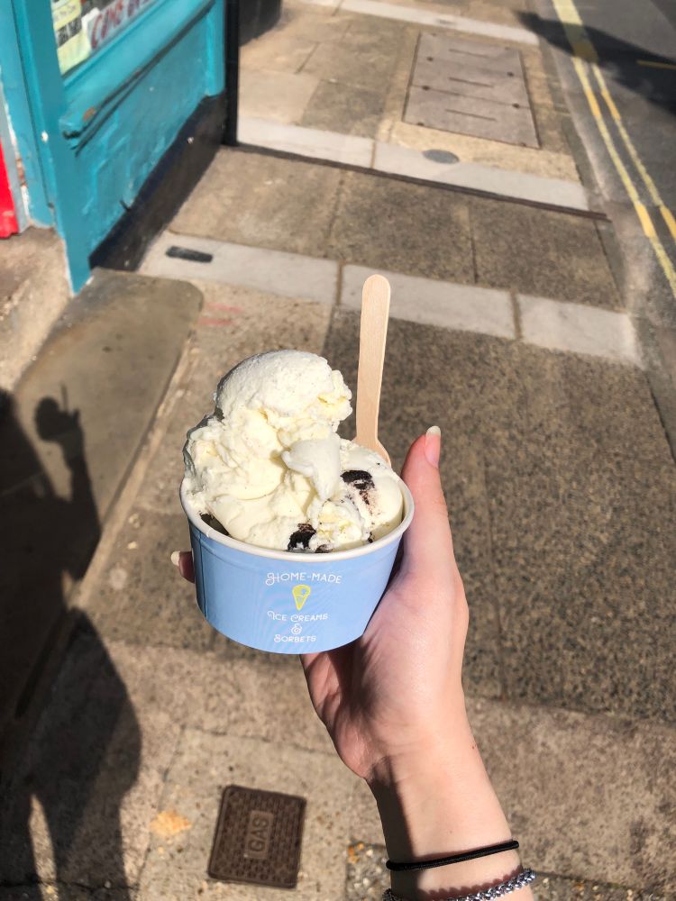 My hand holding a small tub of Oreo and vanilla ice cream 