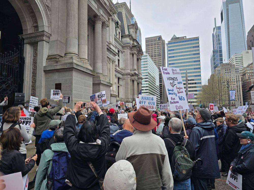 More protesters gathered in front of City Hall, Philadelphia. Many of them are holding up "Hands Off" signs and are looking towards the main coordinator in the far end.