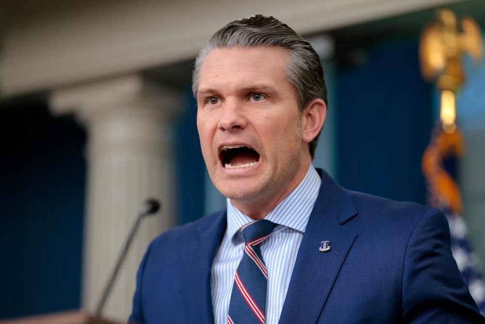 Pete Hegseth shouting with his mouth seemingly stretched open 