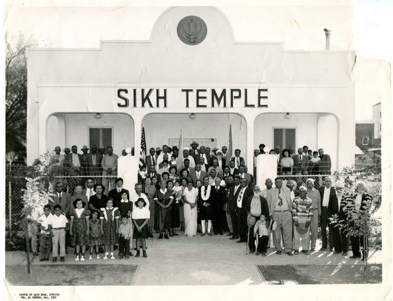 A black and white picture of a crowd posing in front of a building labeled "Sikh Temple" in El Centro, CA in the 1950s.