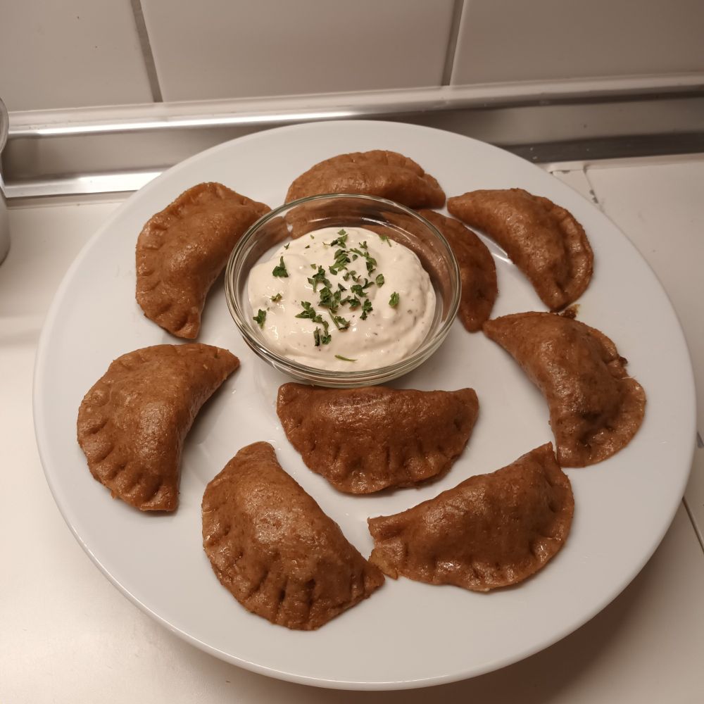 Vegane Gemüse Dumplings auf einem weißen Teller und einer Schale mit Sour Creme Dip in der Mitte.