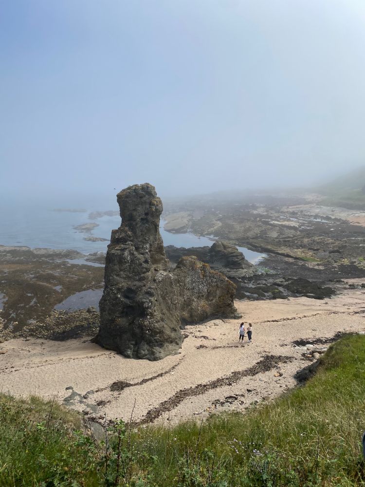 huge cylindrical rock on the coast of Scotland with fog and rocky shores in the background 
