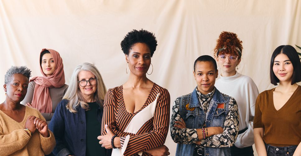 A multi-cultural group of women, varying in ages, all staring directly into the camera with pleasant expressions.