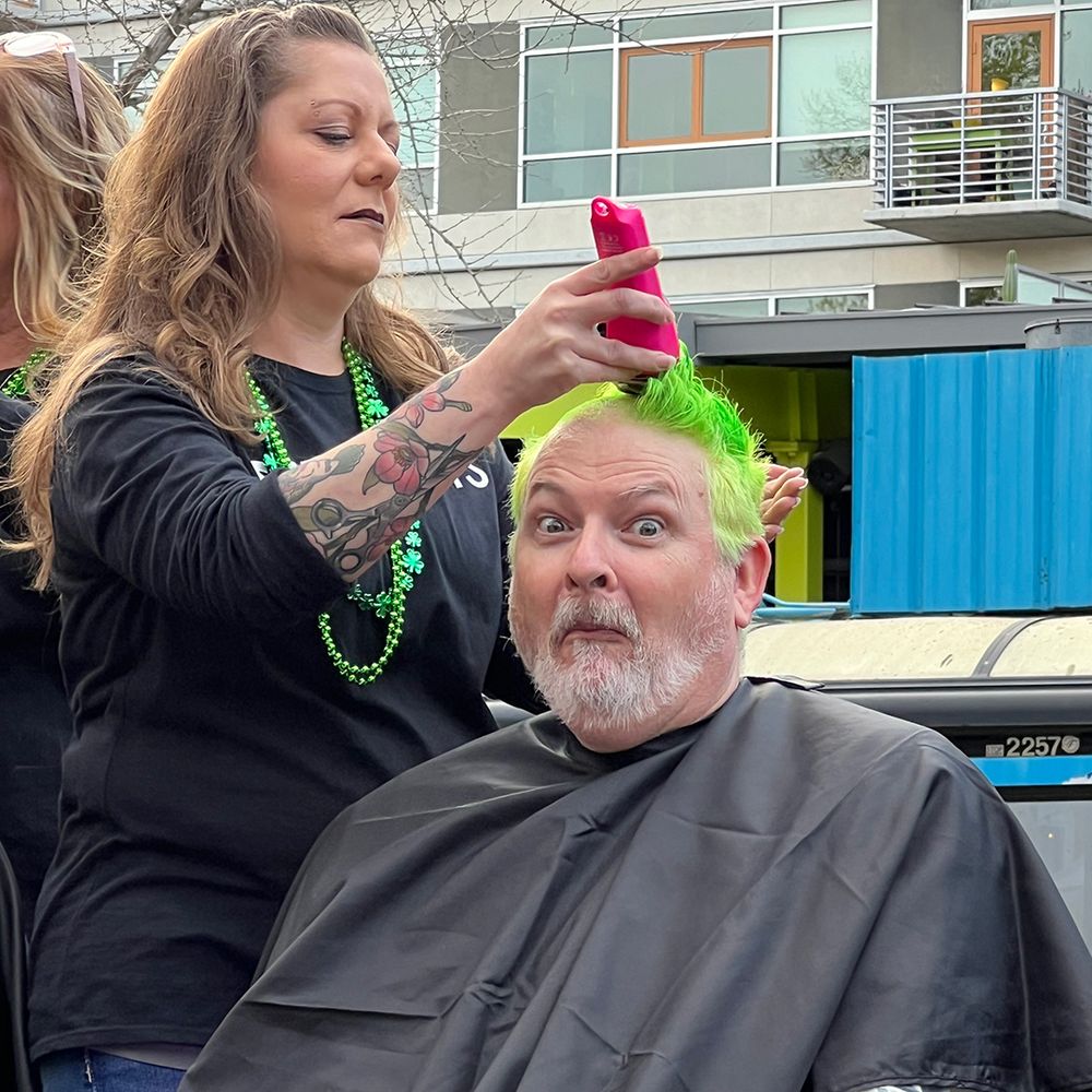 Man with dyed green hair is having his head shaved for St. Baldrick's charity.