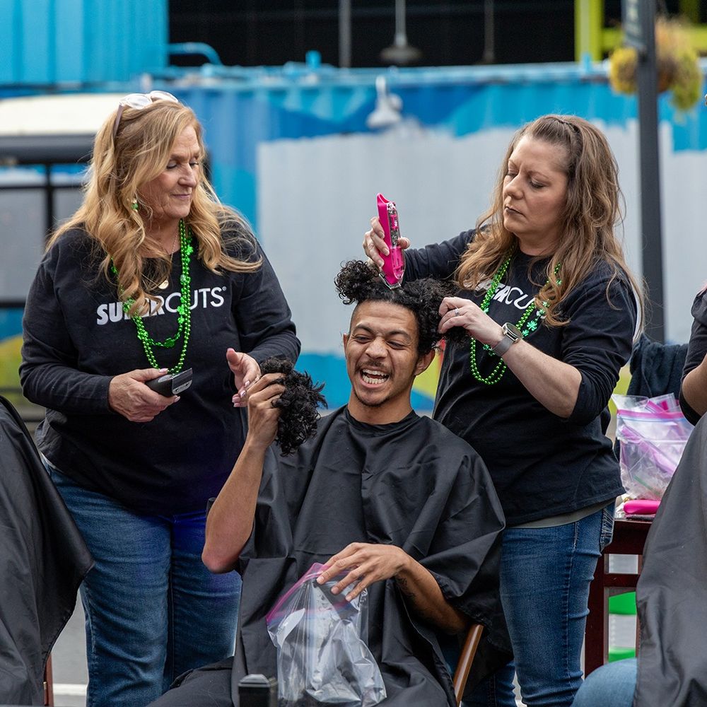 A Black man laughs as his head is being shaved for St. Baldrick's charity fundraiser.