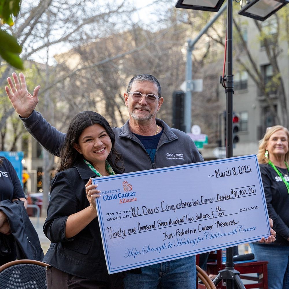 A young woman is presenting a check to an older man. The check is for the amount of $91,702.06. They are smiling.