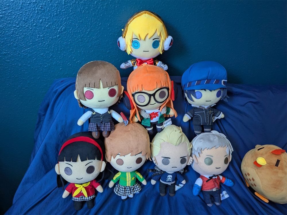 Photo of eight Persona plush toys from Sanshee stacked in a pyramid. A brown chicken from Stardew Valley peeks in from the side.