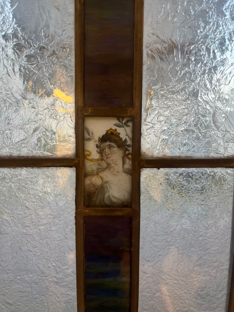 old vintage bathroom window stained glass panel of a woman in the middle with brown hair and a gold crown