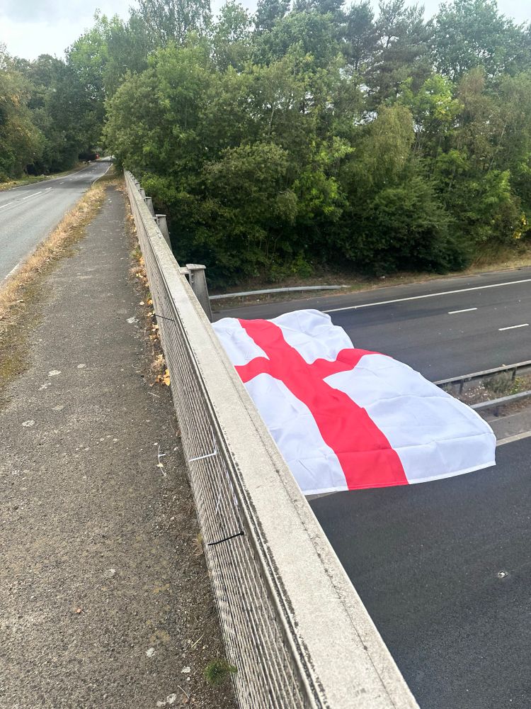 A red cross flag, now a sign of fascism in the UK, briefly from a motorway bridge. 