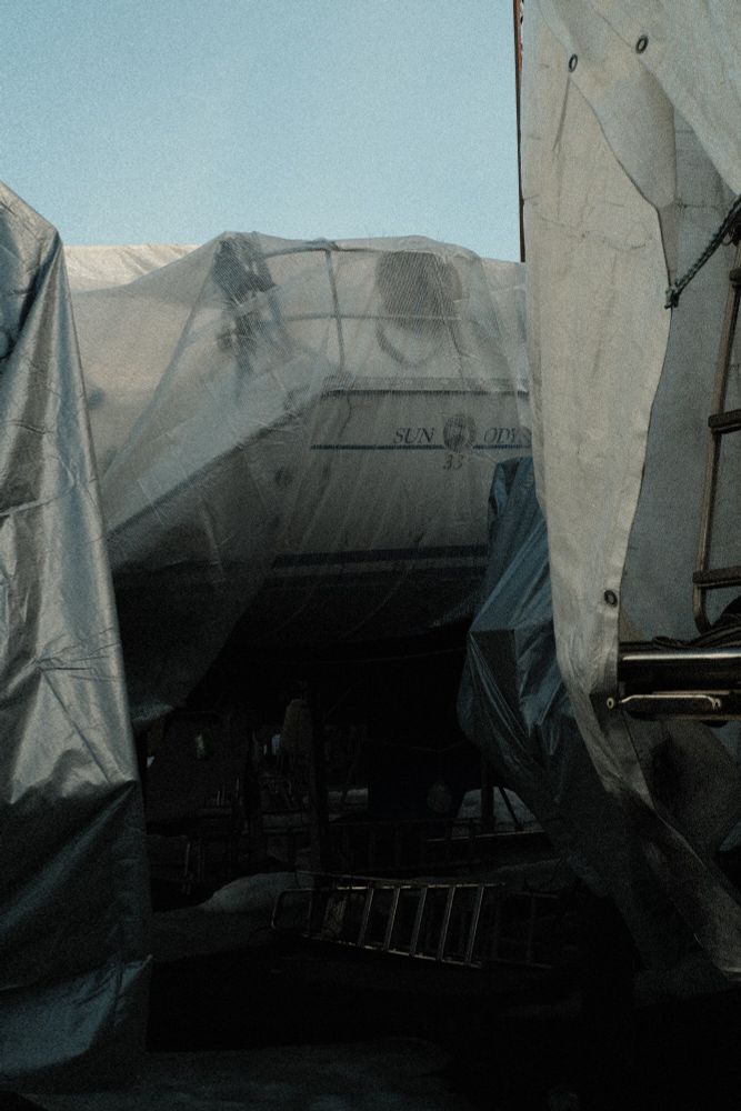 A shot of three draped boats and a ladder that has fallen down which shimmers in the shadows.
