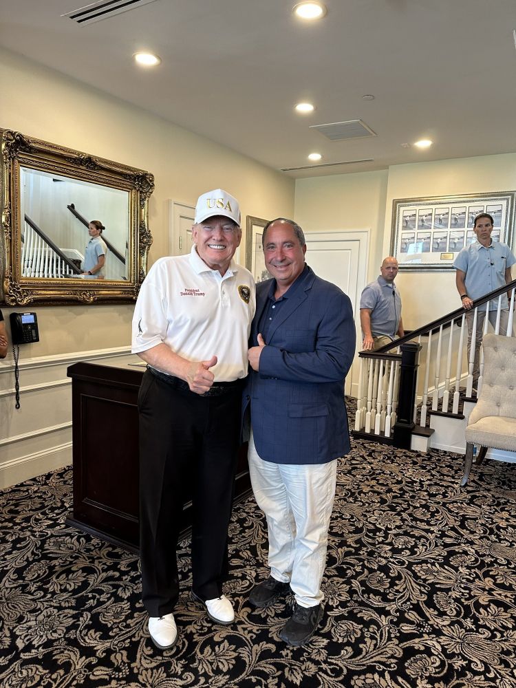 the photo of donald trump giving a thumbs up with a supporter in an upscale-looking landing, looking grey and ashen
