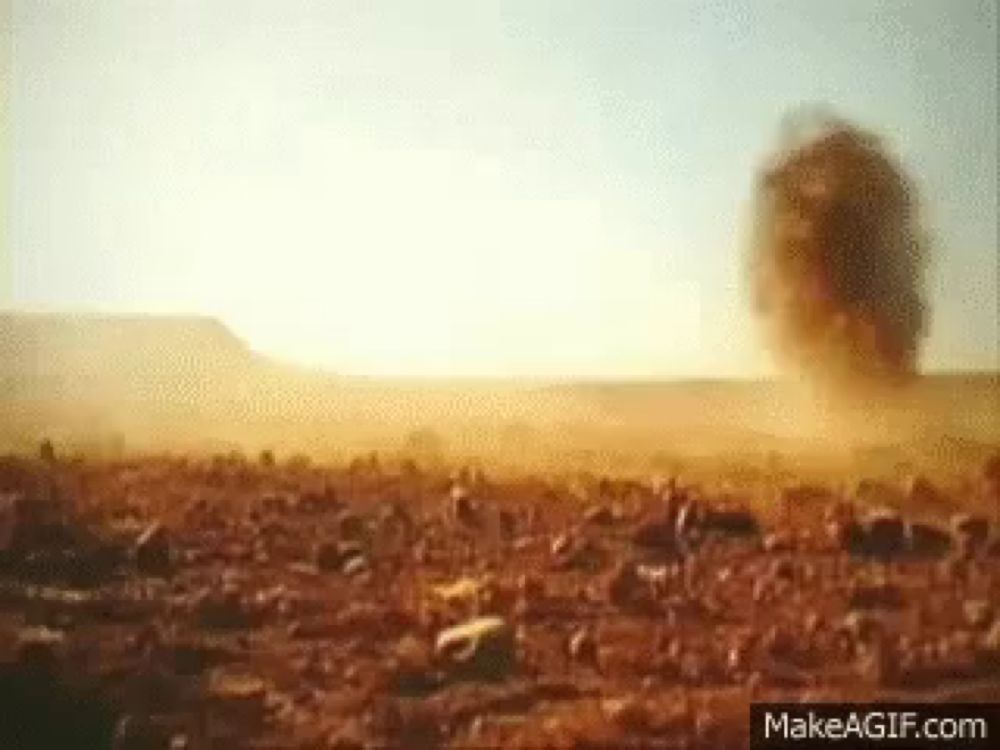 a dust storm in the desert with a large rock in the foreground .