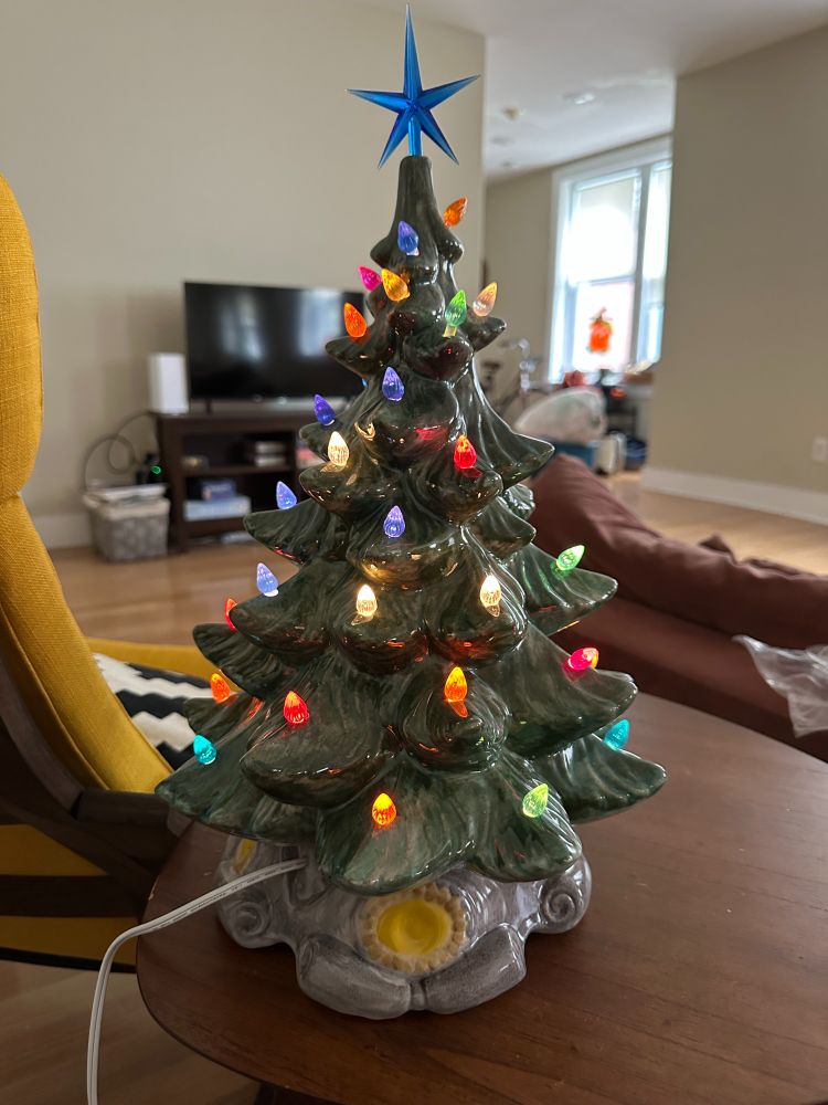 A green ceramic Christmas tree with multicolored lights and a blue star on top. Living room in the background.