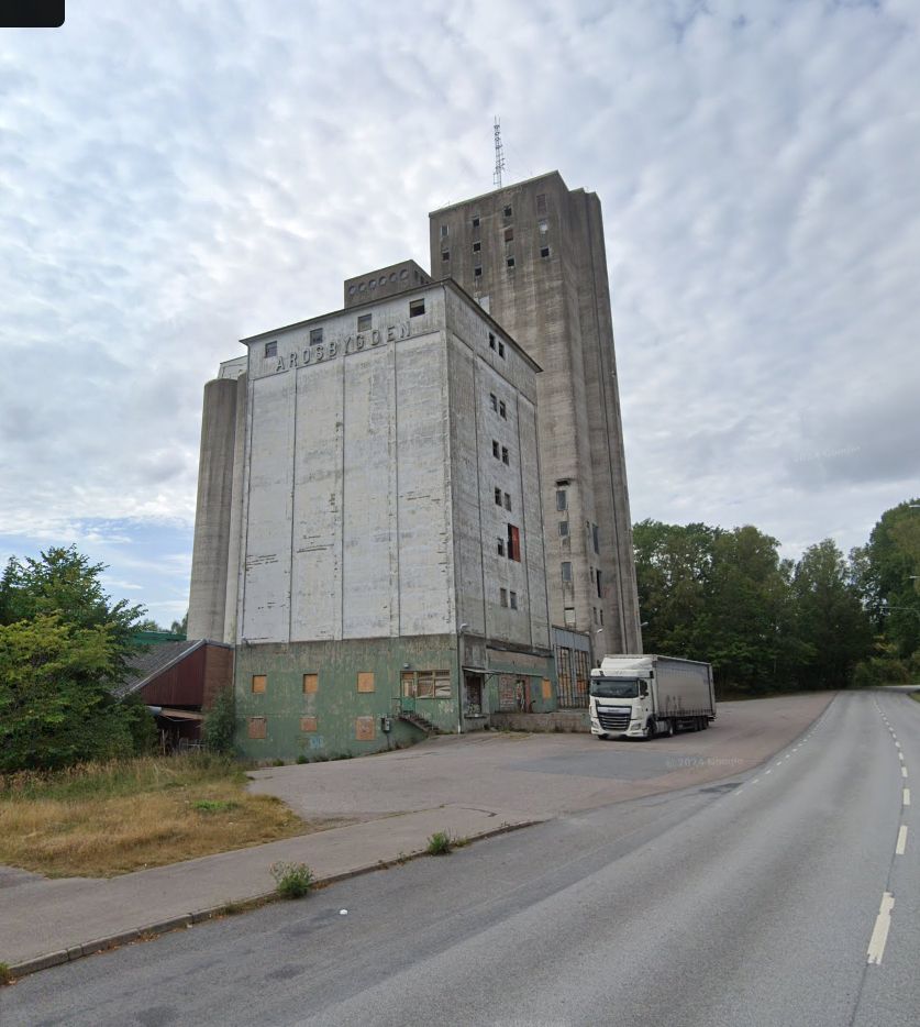an abandoned factory building off the side of a road. a semi truck is parked next to it 
