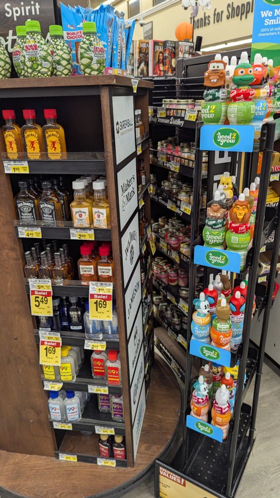 A rotating rack with various small bottles of liquor next to a rack of kiddie juices with Disney caps