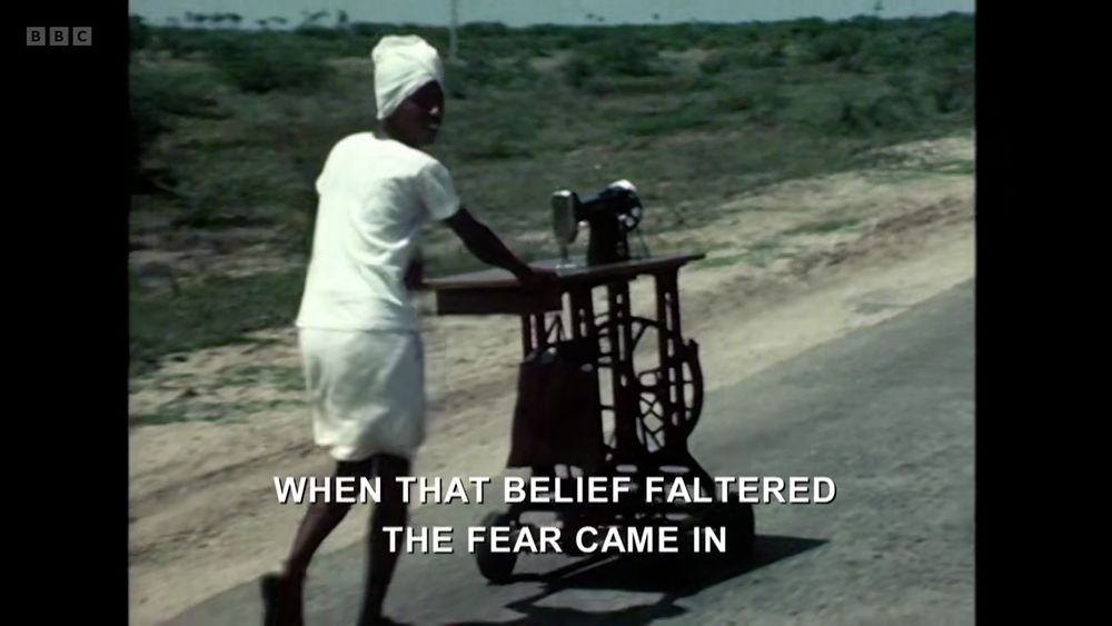 From Adam Curtis' "Shifty: Living in Britain at the End of the Twentieth Century", another image of an Indian boy rolling a sewing machine down a rural road, now looking back at the camera over his shoulder; titles across the bottom read: "When that belief faltered the fear came in."