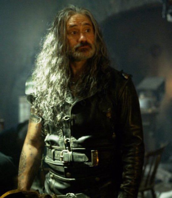 Edward Teach in season 2 episode 8 of Our Flag Means Death, wearing his Blackbeard leathers, standing in Spanish Jackiez and looking at Stede out of frame with an impressed expression