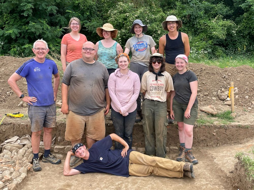 Photo of 9 archaeologists standing in a trench.