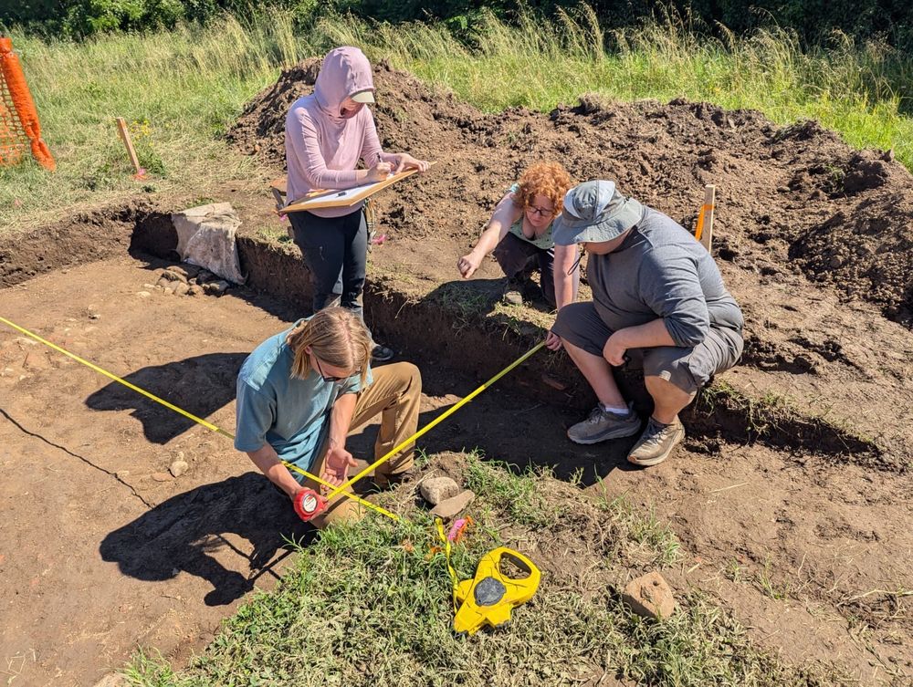 Three students draft a trench plan while the supervisor looks on.