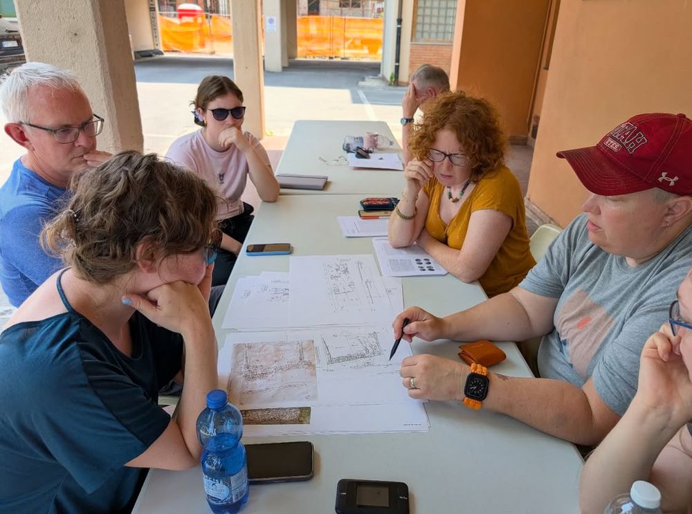 A group of people sit around a table looking at trench plans. 
