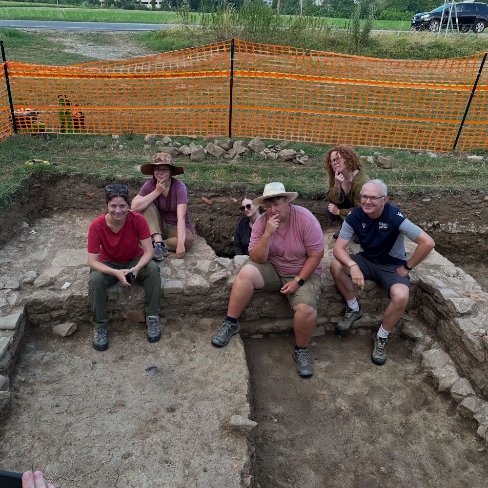 A photo of six people sitting on the walls in a trench. 