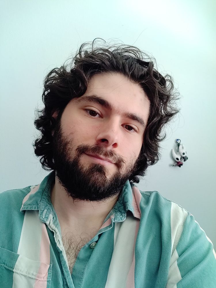 Another selfie. 2 Hollow Knight keychains hang on the wall behind.