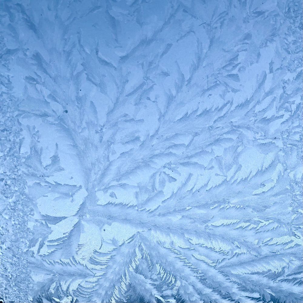 Eisblumen an einem Dachfenster: Man ahnt den blauen Himmel hinter der Eisschicht. 
