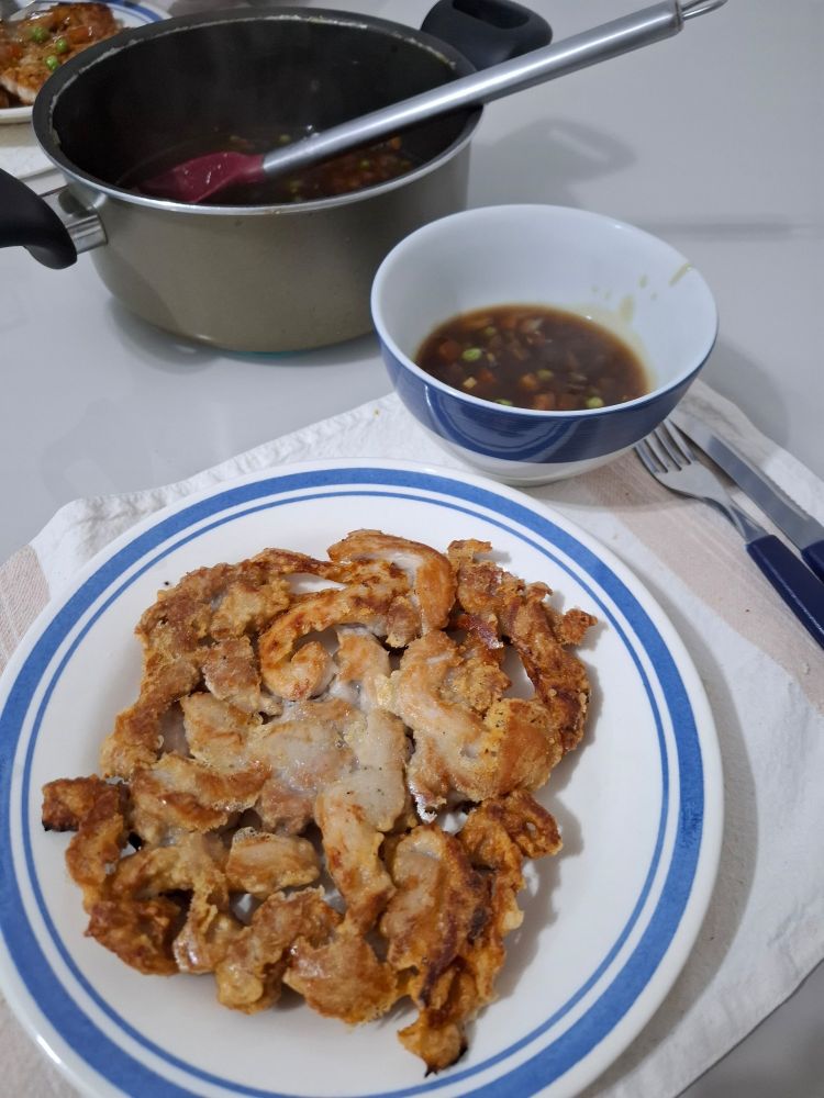 Prato com panqueca frita feita com tiras de lombo suíno empanados com molho agridoce escuro com legumes.
