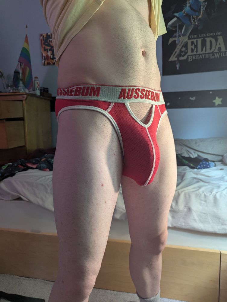 I'm standing in the middle of my room, wearing a yellow shirt (which I'm lifting with my teeth) and a red Aussiebum jockstrap (which is bulged the fuck out by my massive dick).