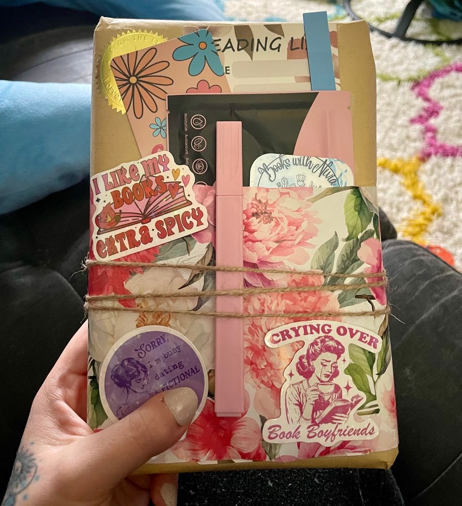 An image of a wrapped Blind Date with a Book. There are extra goodies (stickers, highlighter, bookmark, eye masks, reading log) attached.