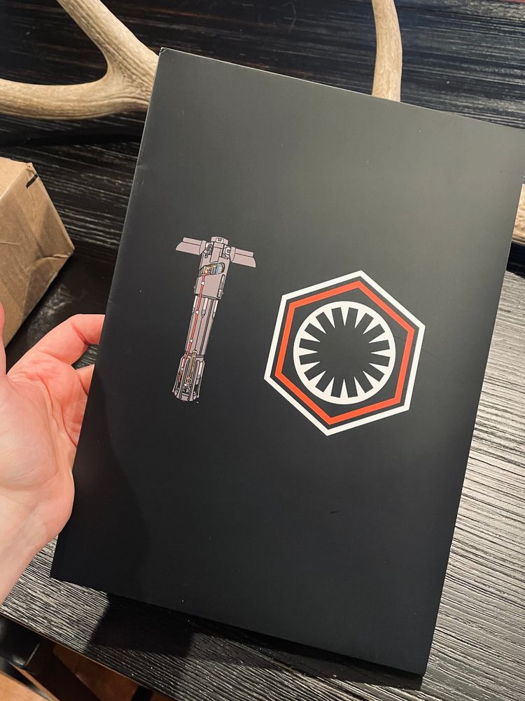 Cover of the Careful Ren zine with Kylo's lightsaber and the First Order logo, held above a black table