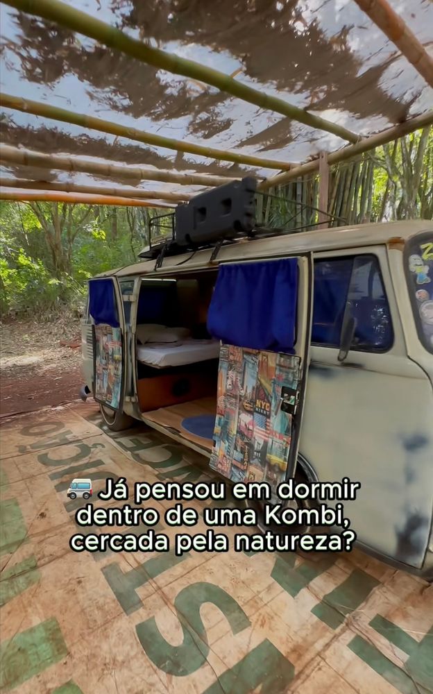 Pousada com uma kombi detonada, com pintura manchada e adesivos como "dormitório", o chão de terra batida está  coberto por uma lona de outdoor bem suja, a cobertura é feita também de lona com estrutura de bambus...
Legenda "🚐 já pensou em dormir dentro de uma kombi, cercada pela natureza?"