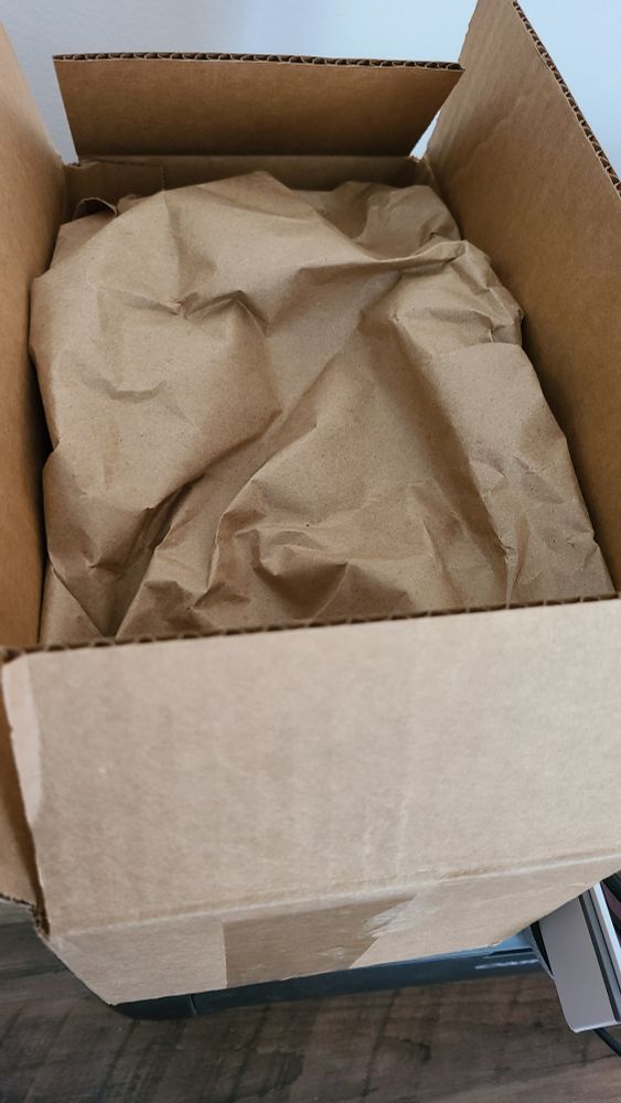 An open shipping box with brown wrapping paper obscuring the contents of the box.