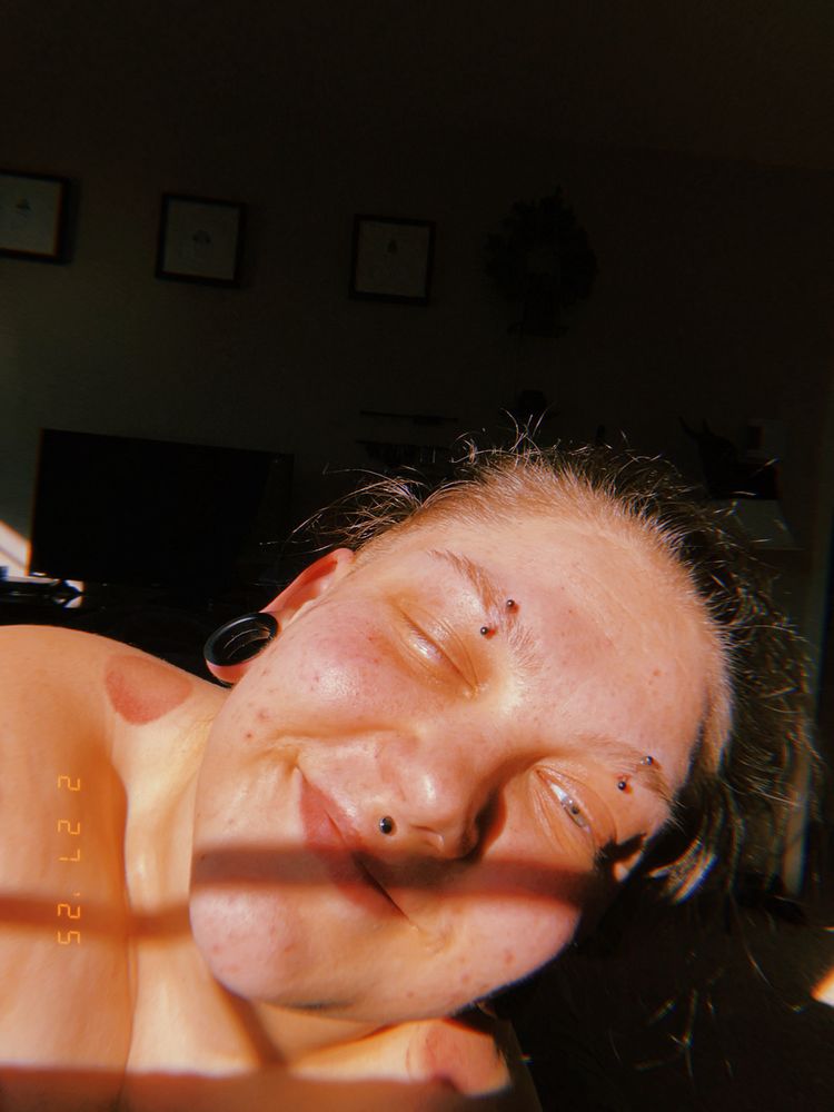 A selfie of me. I have bed head and my hair is tied back, one of my eyes is closed and the other is hardly open, I have a small smile one might call a smirk. I am shirtless but the picture doesn’t go far below the shoulders. The shadow pattern from the window is covering a horizontal line across the middle of my face. 