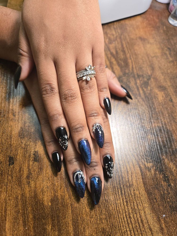 Medium almond nails. Silver moons and stars ain't a black background on the pointer nails. Flat black on the pink and thumb nails and silver stars and gems on the nail lining the cuticle dripping down the nail set over a shimmery blue cat eye polish over black. Topped with a shiny top coat. 