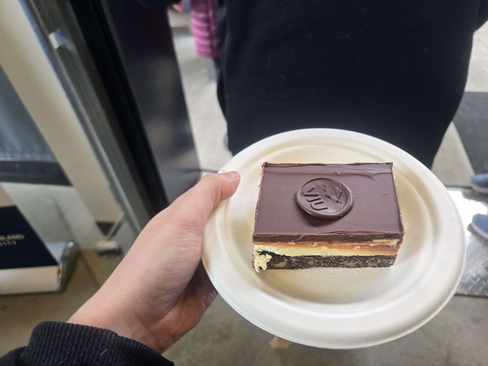 A photo of a Nanaimo bar: a Canadian dessert made with a chocolate nut base, custard filling, and topped with chocolate ganache. It has a chocolate seal reading "VIU"