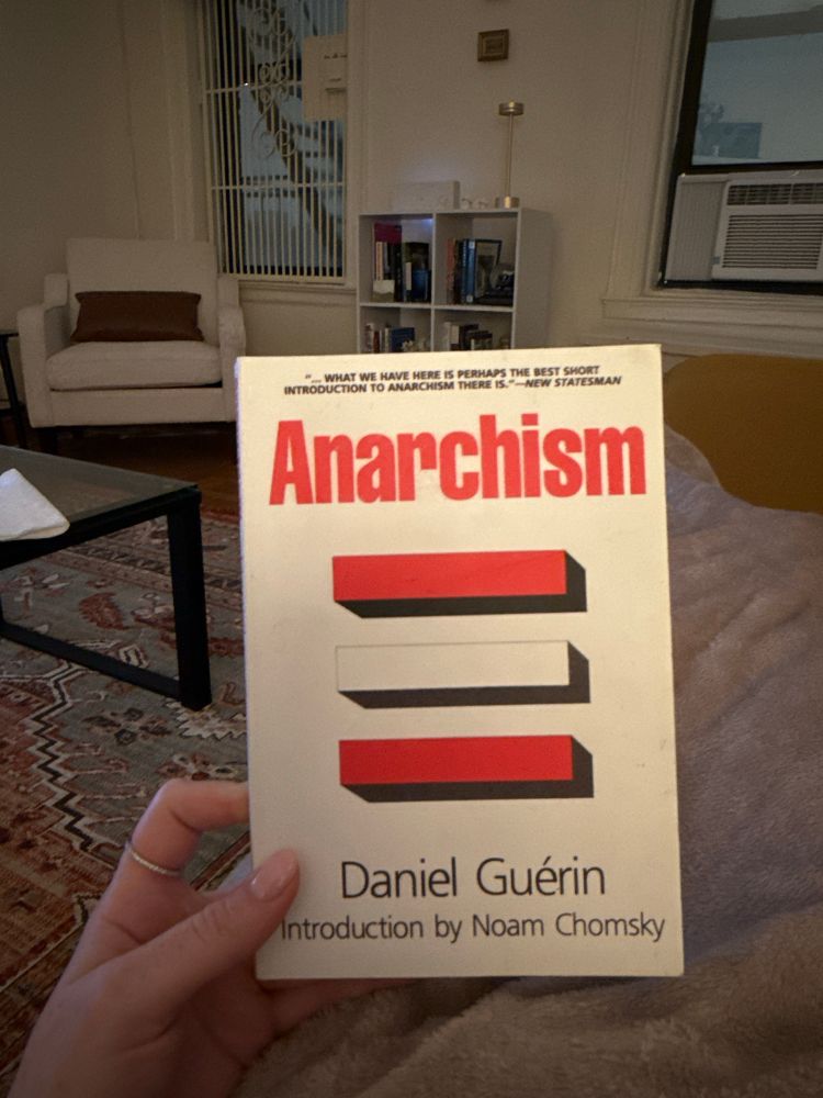 Holding a book on the couch, Anarchism by Daniel Guérin with an introduction by Noam Chomsky 