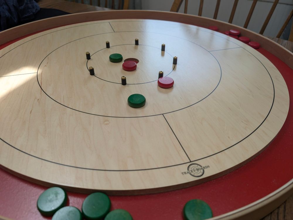 Tam Crokinole board with red gutter. Green and red discs on it. Tracey Boards logo on the playing board outside edge. 