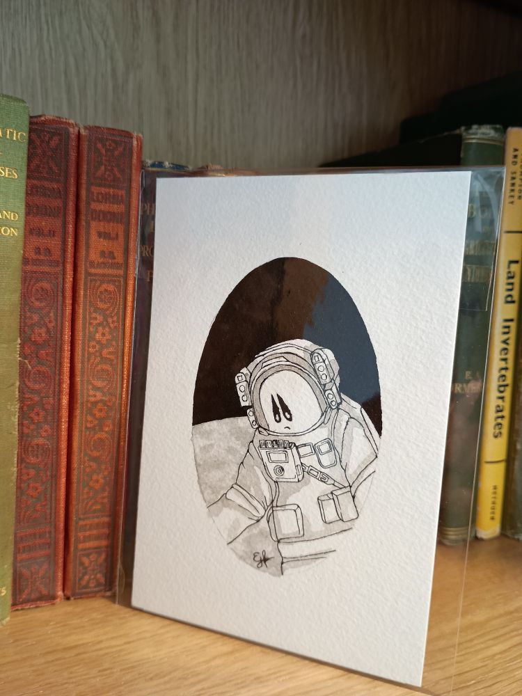 An original A6 black and white ink illustration in cellophane on a bookshelf. A ghost in a spacesuit with the moon visible behind them.