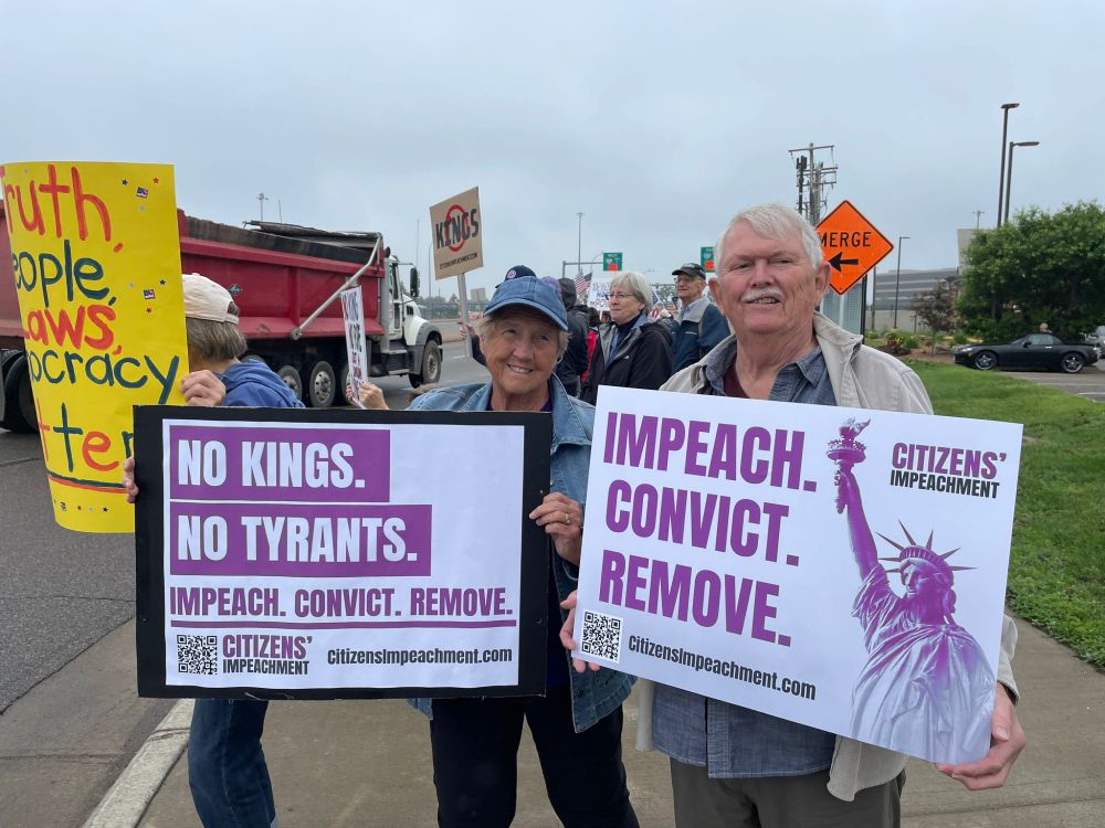 two citizens holding signs that say Impeach, Convict, Remove and No Kings, No Tyrants