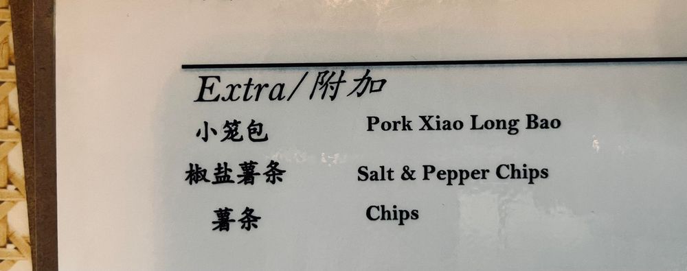 Part of a restaurant menu. Text:

Extra / 附加.
小笼包 Pork Xiao Long Bao.
椒盐薯条 Salt & Pepper Chips.
薯条 Chips.
