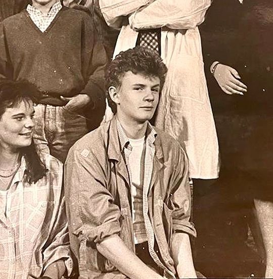 Charles edwards in 1985. He is looking at the camera with a cheeky smirk and raised eyebrow.