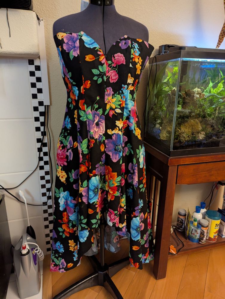 A dress in the middle of being made, hanging on a dress form, in a floral print on black. 