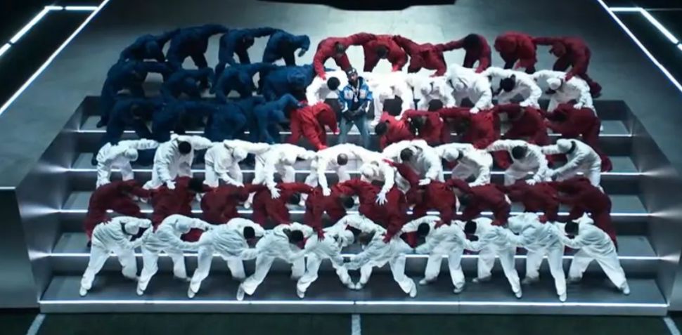 Kendrick Lamar performing at the Super Bowl half time show, standing in the center of an all Black groups of dancers in red, white, and blue, arranged like the American flag.