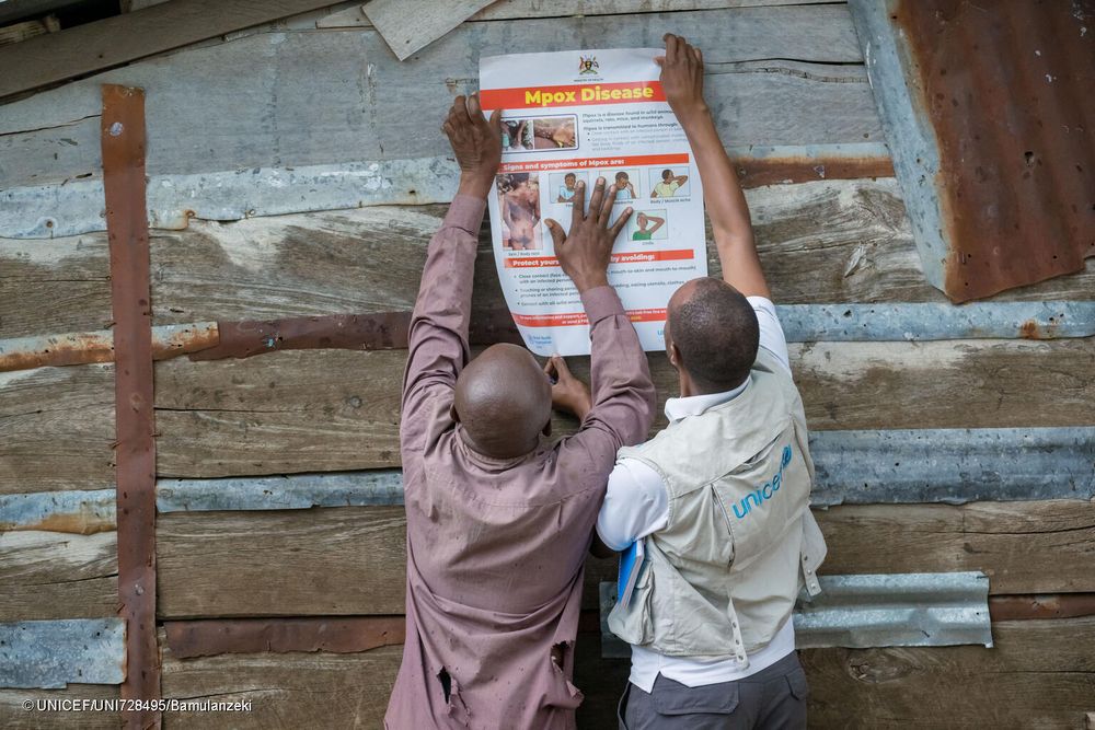 A community health worker and UNICEF field staff put up posters with mpox messaging in order to increase community awareness about mpox.

© UNICEF/UNI728495/Bamulanzeki
