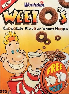 Derek - a young cartoon boy with small blonde hair sticking upwards, blue dot eyes and a head resembling Wallace's; wearing grey fingerless gloves (not pictured), a red and white bomber, jeans and red and white shoes - on an early box of Weeto's, chocolate flavour wheat hoops