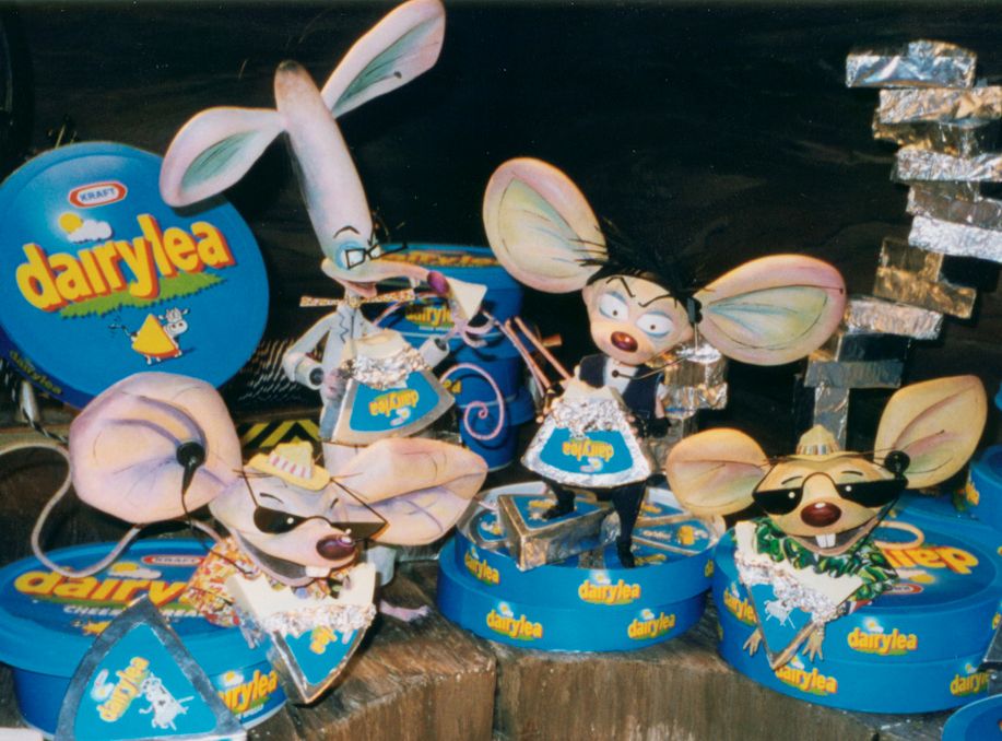 Puppets of the Dairylea mice built by Mackinnon & Saunders: Clockwork, a mad scientist/inventor mouse wearing glasses and a labcoat and sporting a curled tail and a long head with large ears and strands of hair at the top and a face at the bottom; Dexter, who has black hair brushed to the side, a black leather jacket, a white vest and black trousers and shoes, sporting a zig-zag tail; and the Miami Mice, two nearly identical mice wearing sunglasses, summer hats, patterned shirts and striped red shorts