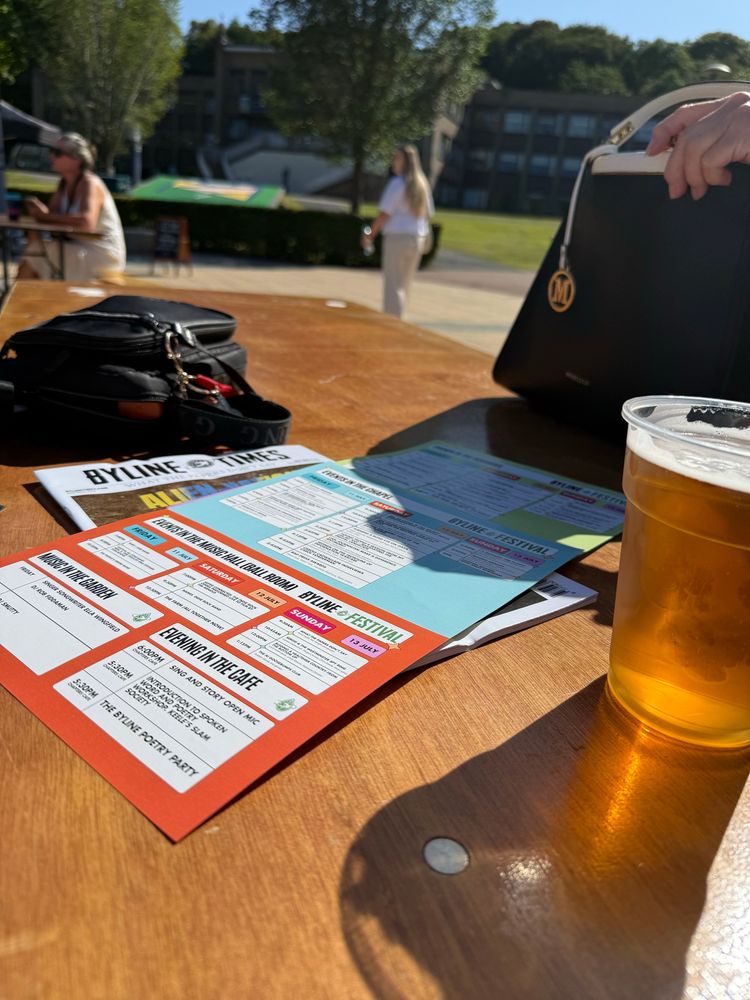 Photo of a sunny table with a pint and the Byline Festival schedule sheet next to it at Union Square at Keele University. 
