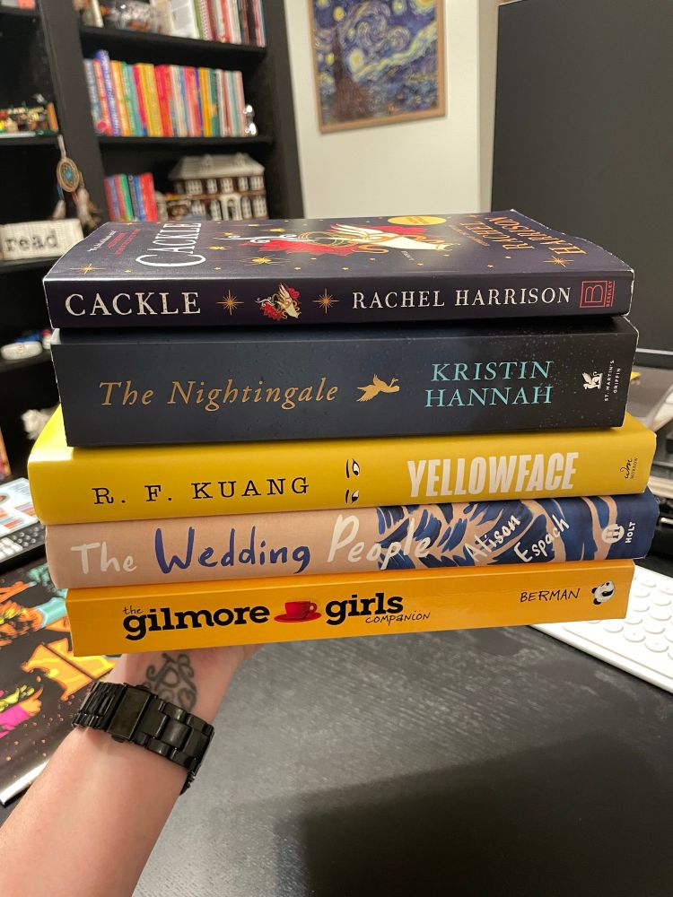 Stack of books. In order from top to bottom: Cackle by Rachel Harrison, The Nightingale by Kristin Hannah, Yellowface by R. F. Kuang, The Wedding People by Alison Espach and The Gilmore Girls Companion by A. S. Berman. 
